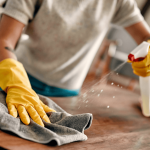 Person cleaning a table with a clothe and yellow gloves to remove dust