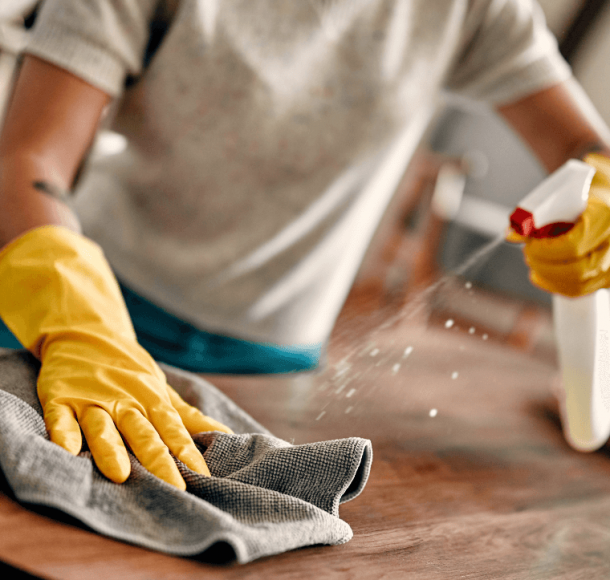Person cleaning a table with a clothe and yellow gloves to remove dust