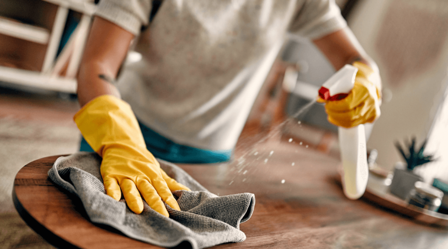 Person cleaning a table with a clothe and yellow gloves to remove dust