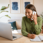 Woman talking by phone in front of her laptop in a livingroom looking for a Cleaning Services company