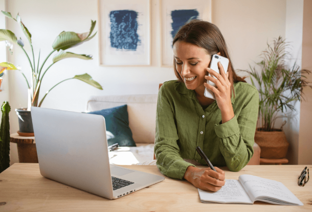 Woman talking by phone in front of her laptop in a livingroom looking for a Cleaning Services company