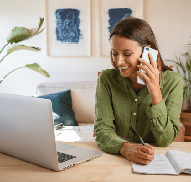 Woman talking by phone in front of her laptop in a livingroom looking for a Cleaning Services company