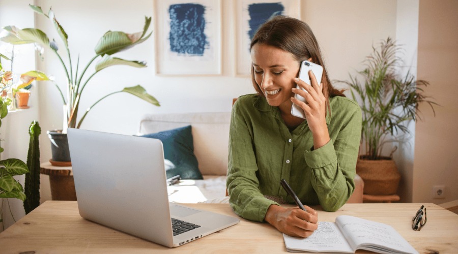 Woman talking by phone in front of her laptop in a livingroom looking for a Cleaning Services company