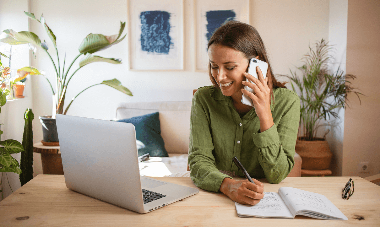 Woman talking by phone in front of her laptop in a livingroom looking for a Cleaning Services company